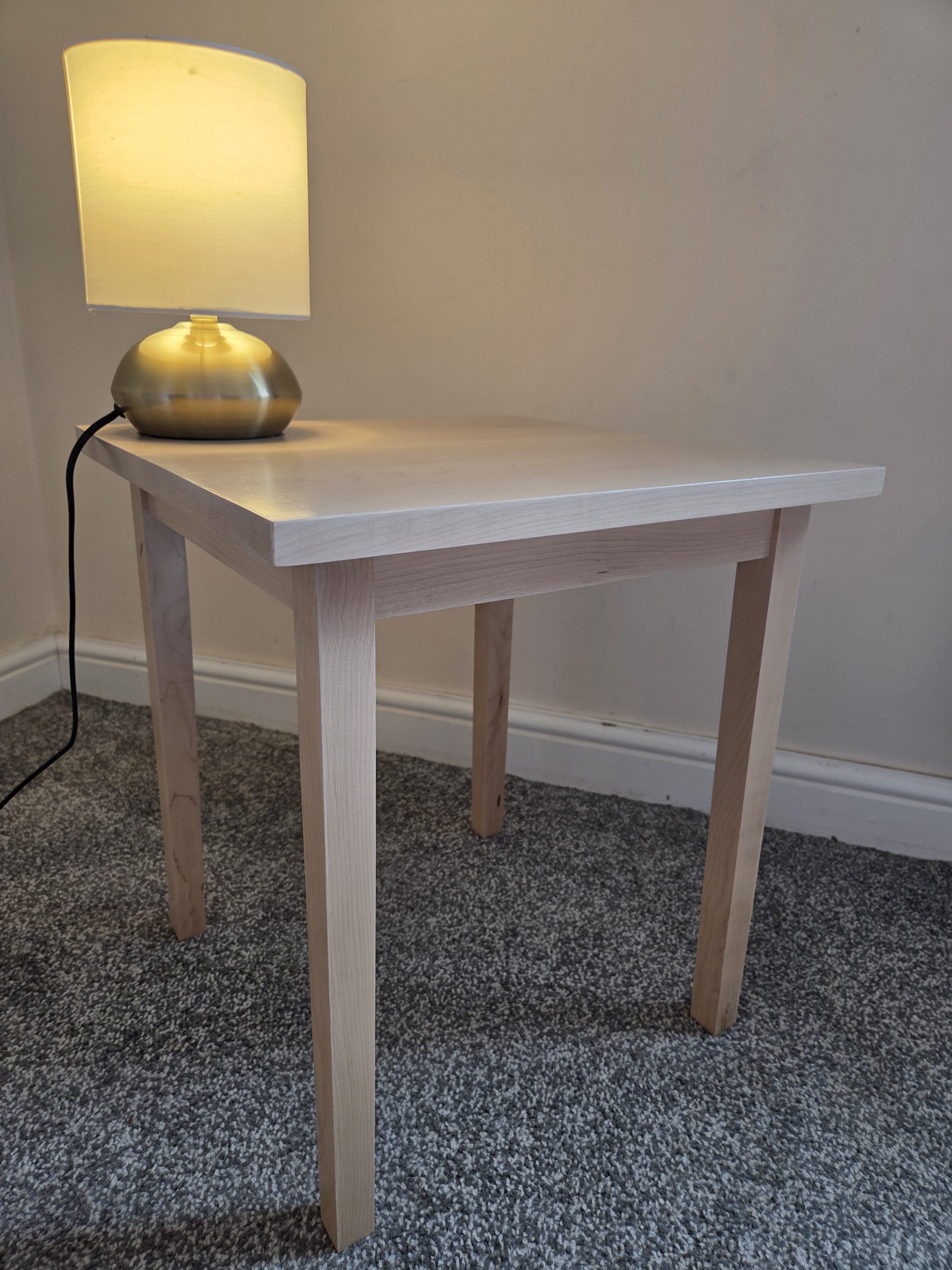 Elegant handcrafted wooden side table with a smooth natural finish, designed for timeless simplicity and everyday function. Shown in a cozy interior setting with a warm-glow lamp, this piece embodies the craftsmanship and sustainable ethos of Wood Furniture by Peter.
