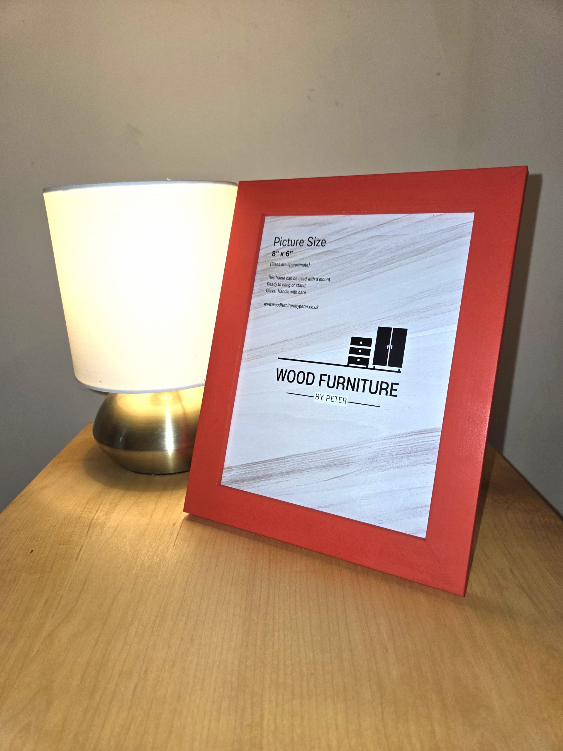 Handcrafted wooden table featuring a soft-glow lamp with a metallic base and white shade, beside a red picture frame displaying “WOOD FURNITURE BY PETER” branding. A warm, minimalist setup showcasing artisan craftsmanship and elegant home decor.